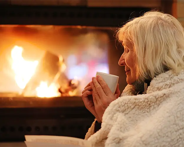eldre dame koser seg med kaffe foran peisen
