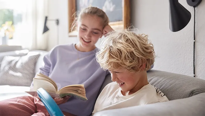 Søsken som sitter i sofaen hjemme